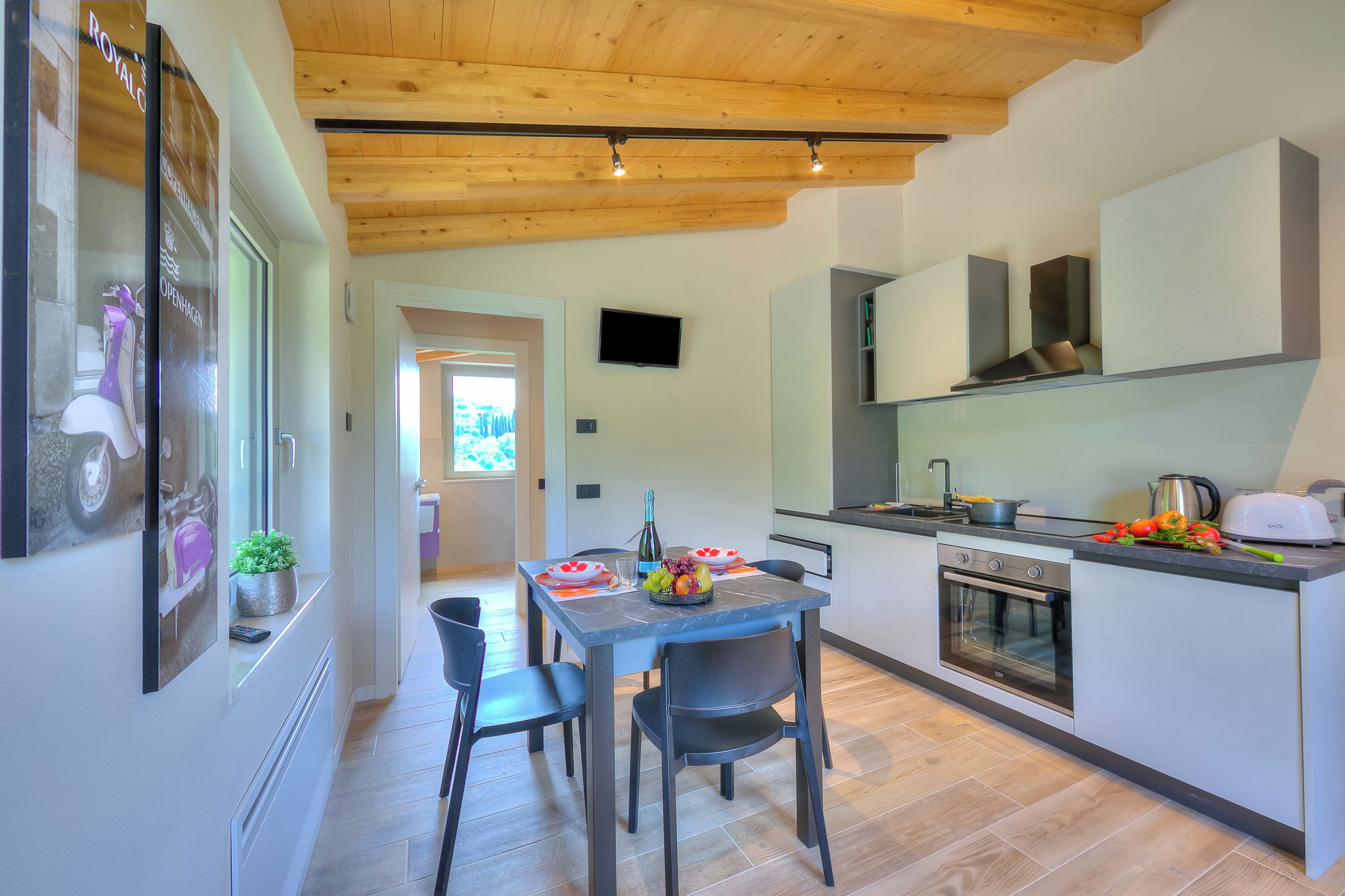 A modern kitchen with a built-in oven, a dining table with chairs, and a TV mounted on the wall.