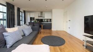 A modern living room with a sofa, a TV, and a kitchen in the background. - Central and Modern 1 Bedroom Flat in Bermondsey (London)