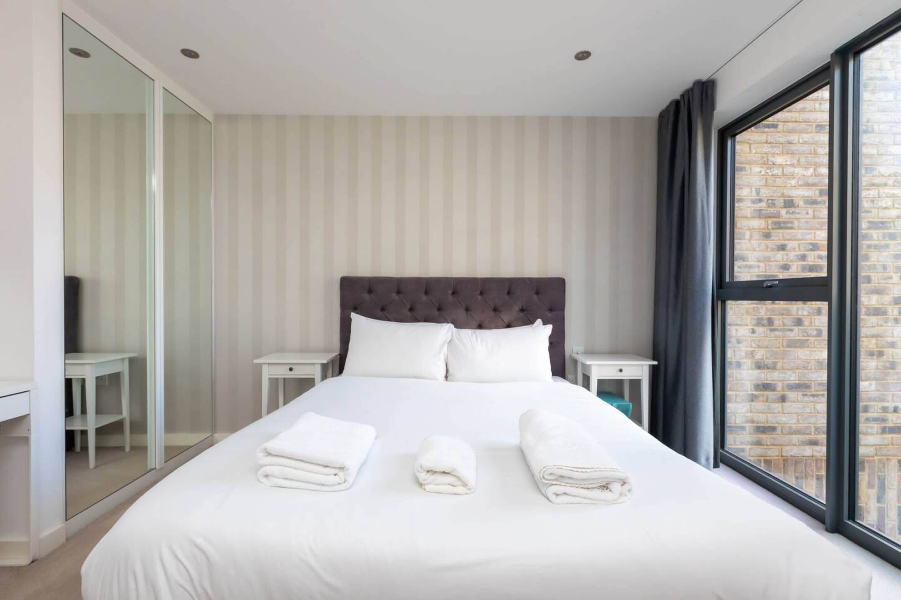 A hotel room with a large bed, a glass closet, and a view of a brick building.