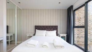 A hotel room with a large bed, a glass closet, and a view of a brick building. - Central and Modern 1 Bedroom Flat in Bermondsey (London)