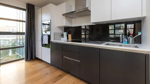 A modern kitchen with dark cabinetry, a stainless steel range hood, and a large window with a view of the outside. - Central and Modern 1 Bedroom Flat in Bermondsey (London)