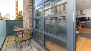 A modern apartment with a sliding glass door leading to a balcony with a wooden table and chairs. - Central and Modern 1 Bedroom Flat in Bermondsey (London)