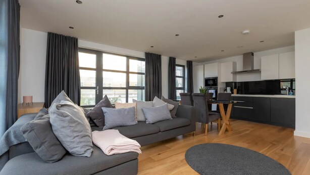 A modern living room with a grey sofa, a dining table, and a kitchen in the background. - Central and Modern 1 Bedroom Flat in Bermondsey (London)