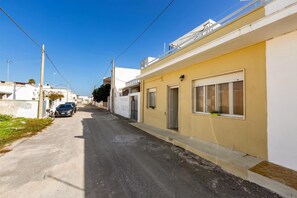 Uma rua estreita com edifícios residenciais, um carro estacionado e uma bicicleta.