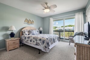 A bedroom with a bed, two bedside lamps, a ceiling fan, a window with curtains, and a view of buildings outside.