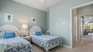 Un dormitorio con dos camas, cada una con una colcha azul estampada con flores, una lámpara blanca y cuadros en la pared.