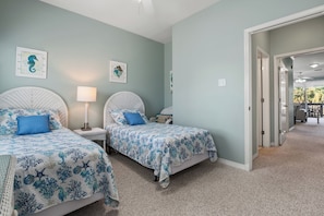 A bedroom with two beds, each with a blue floral bedspread, a white lamp, and framed artwork on the wall.