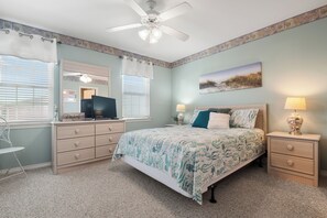 Un dormitorio con cama, cómoda, escritorio, silla, ventilador de techo y ventana con persianas.