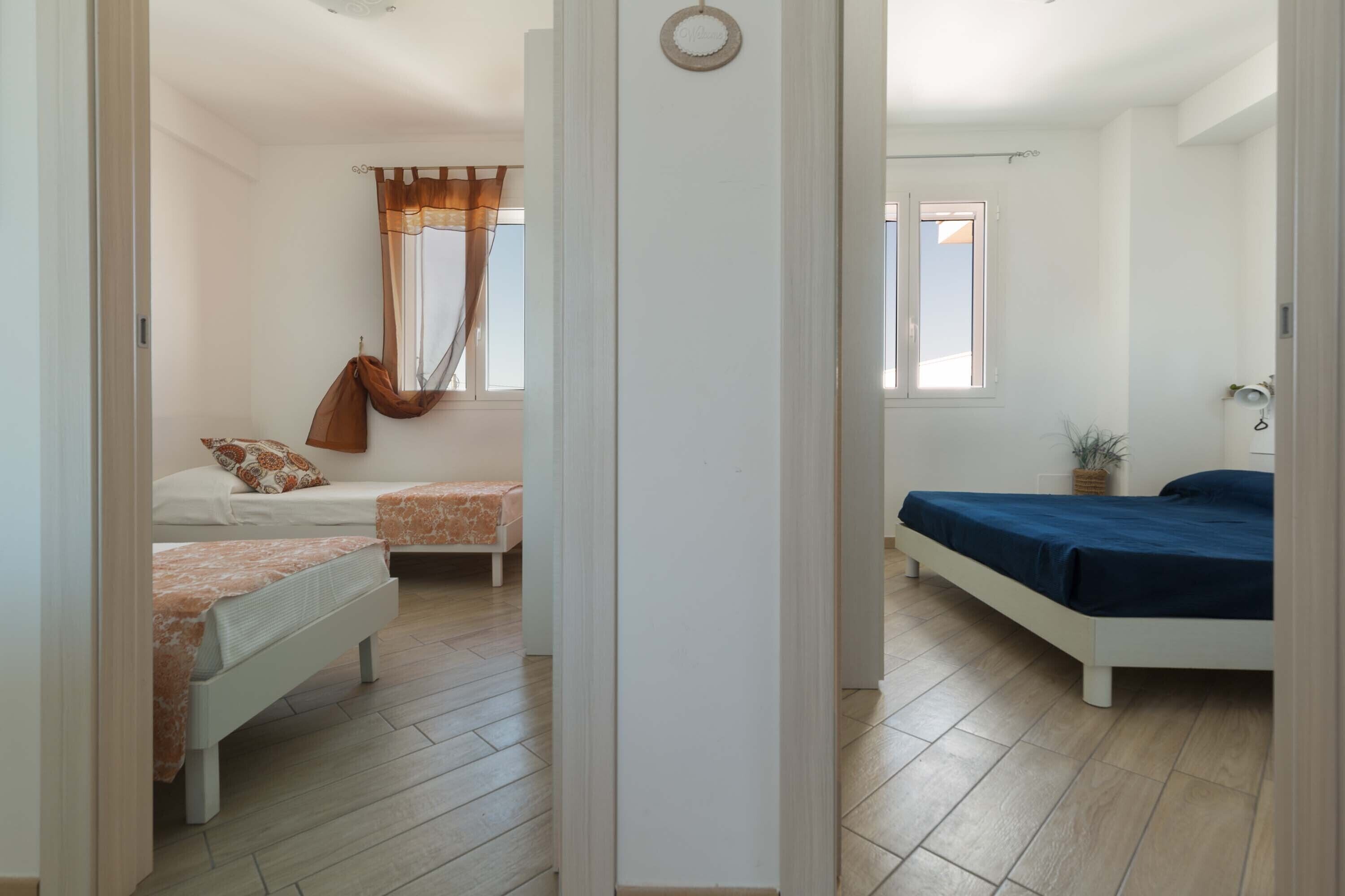 A bedroom with two beds, a window with curtains, and a potted plant.