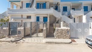 Un edificio blanco de varios pisos con contraventanas azules, una entrada porticada y una escalera que conduce a los pisos superiores.