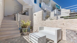 Un espacio exterior moderno con un muro de piedra, un sofá de mimbre blanco y una escalera que lleva a un nivel superior.