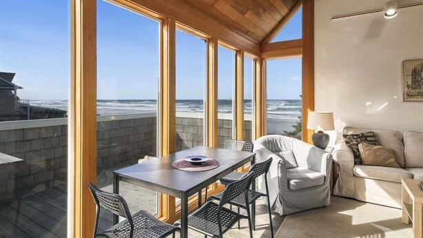 A spacious balcony with a wooden ceiling, large windows offering ocean views, a dining table with chairs, and a sofa.