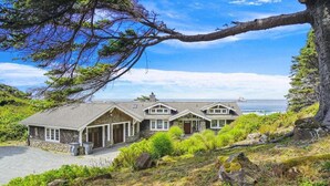 A coastal house with a stone facade, multiple gabled roofs, and a view of the sea. - Cove Beach Lodge - Magnificent Oceanfront! (Arch Cape)