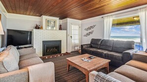 A cozy living room with a fireplace, a leather sofa, a flat-screen TV, and a view of the ocean. - Haystack Close North (Cannon Beach)