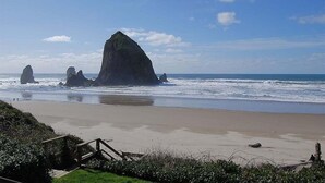 A beach with a large rock formation and a wooden staircase leading down to the shore. - Haystack Close North (Cannon Beach)