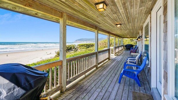A covered porch with a view of the beach, wooden railings, and blue chairs. - Haystack Close North (Cannon Beach)