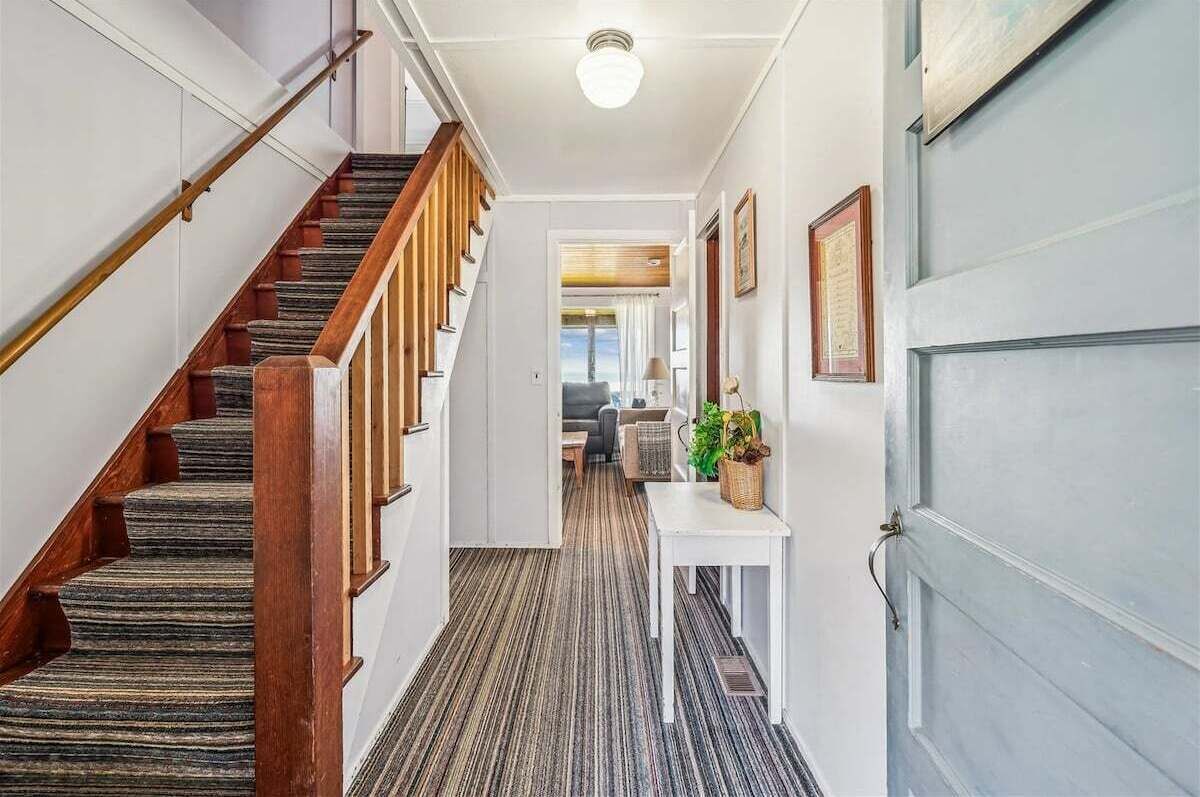 Un couloir avec un escalier en bois, une porte blanche et une petite table sur laquelle est posée une plante.