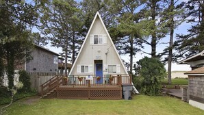 Een driekantig huis met een houten terras, een blauwe deur en een klein portaal.