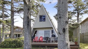 Een driehoekige cabin met een terras, omringd door bomen.