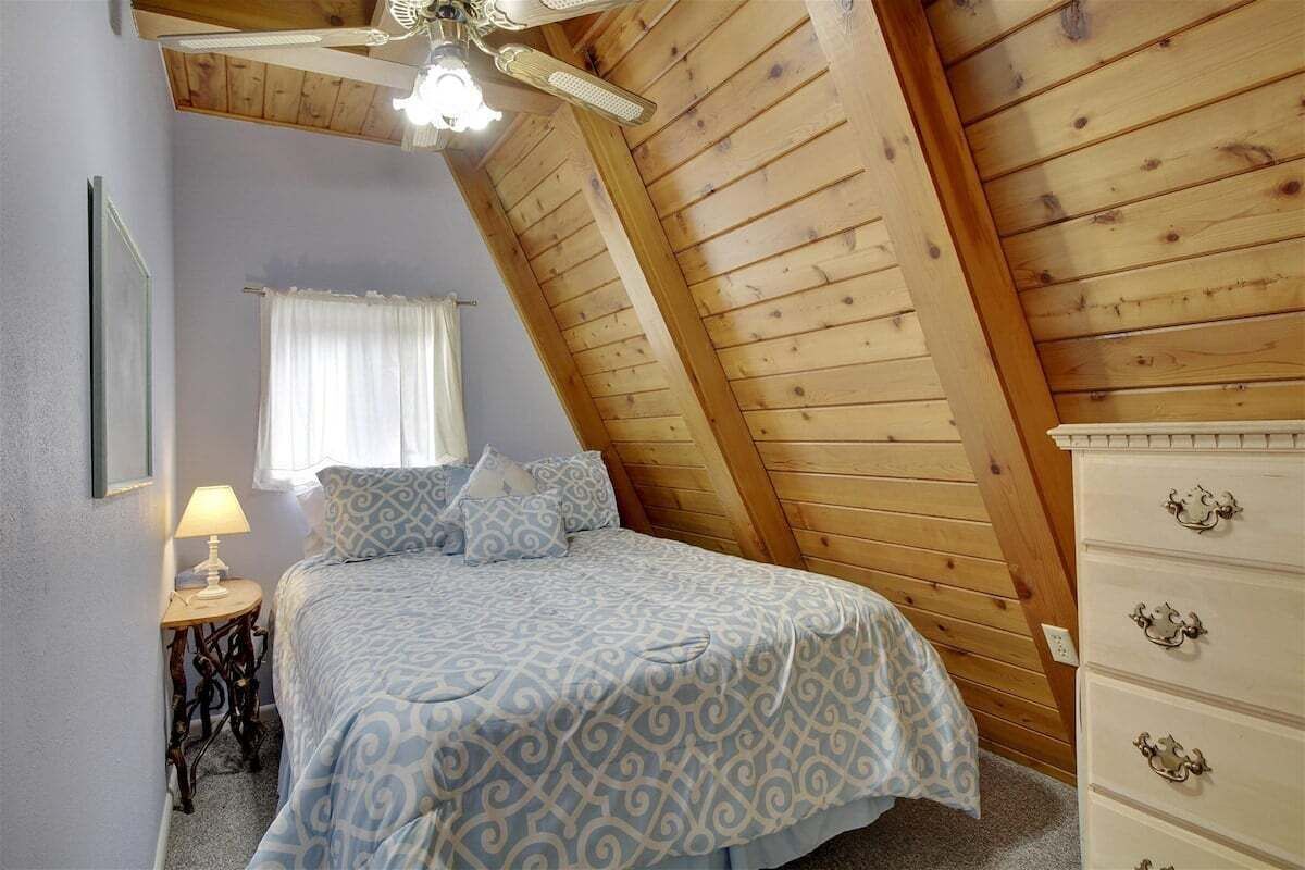Un dormitorio con techo inclinado, una cama con ropa de cama estampada, una mesita de noche con lámpara y un aparador con cajones.