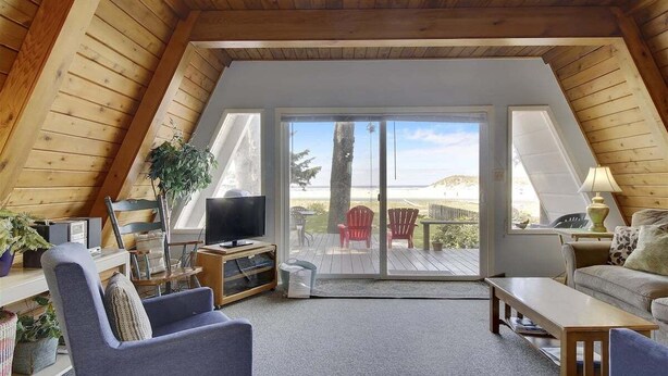 Een gezellige slaapkamer op zolder met een houten schuine dak, een grote schuifglazen deur naar een terras, een televisie en een zithoek met een bank en stoelen.