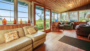 Une pièce chaleureuse avec un plafond en bois, de grandes fenêtres, un canapé en cuir, une table en bois et un fauteuil vert.