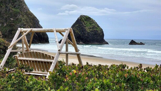 Une balançoire en bois installée sur une plage, avec des falaises rocheuses en arrière-plan.