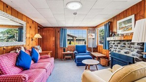 Interior acogedor de una cabaña con detalles de madera, una chimenea de piedra, un sofá, una silla y una mesa de comedor.