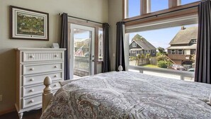 Een slaapkamer met een groot bed, een dressoir, een raam met gordijnen en een ingelijste foto aan de muur.