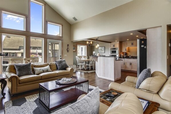 A spacious living room with a sofa, coffee table, and a kitchen area visible through an open doorway.