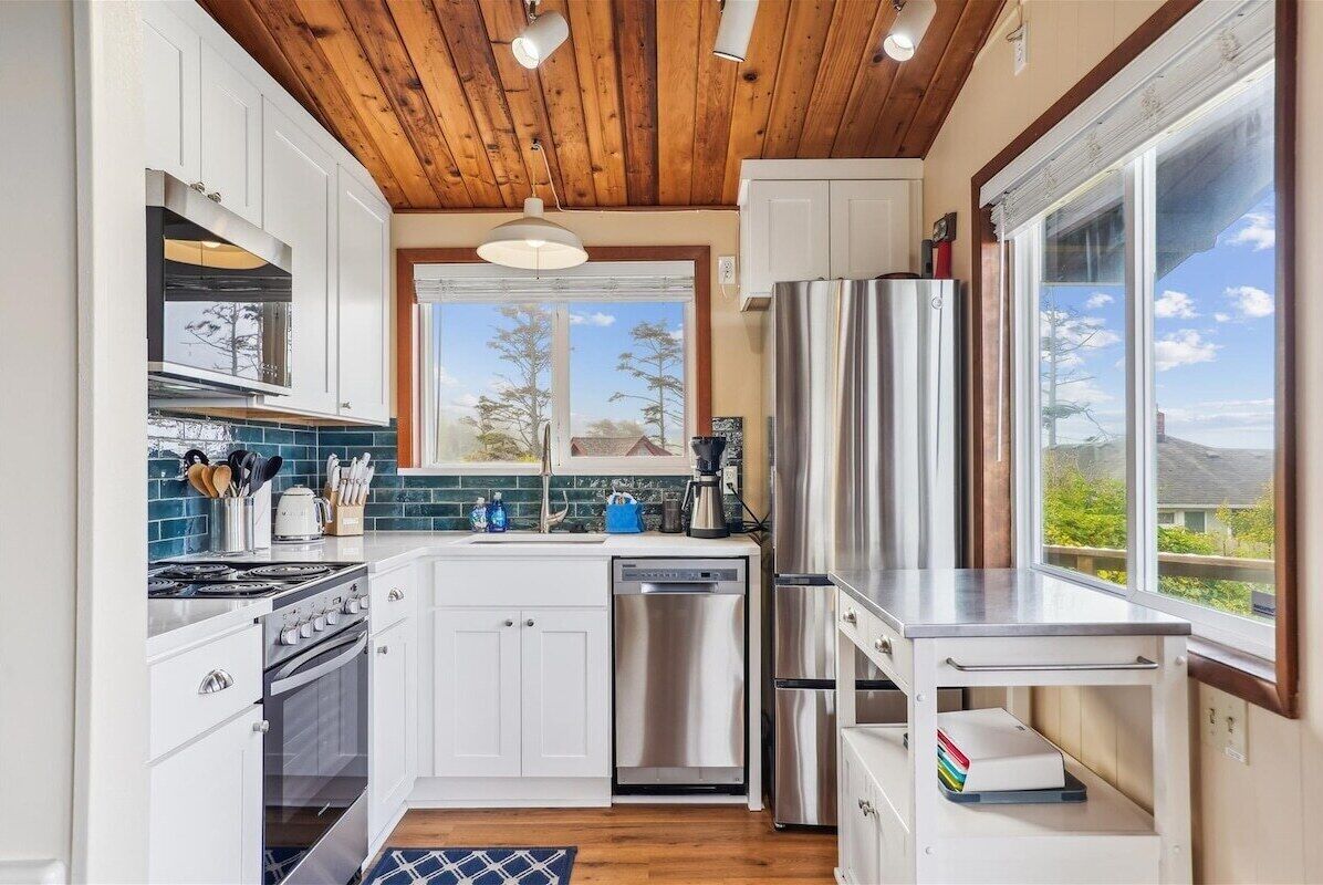 A modern kitchen with white cabinets, stainless steel appliances, and a wooden ceiling.