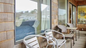 Um deck de madeira com cadeiras e mesa de metal, janelas amplas e um lustre pendurado.