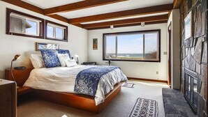 A bedroom with a large bed, wooden beams, a stone wall, and a view of the outdoors. - Beach Haven - Beachfront! (Cannon Beach)