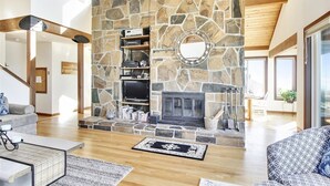 A spacious living room with a stone fireplace, wooden beams, and a large window. - Beach Haven - Beachfront! (Cannon Beach)