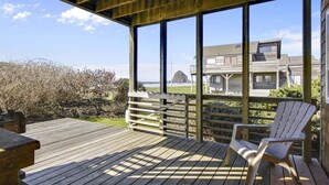 A wooden deck with a view of a building and beach in the background. - Beach Haven - Beachfront! (Cannon Beach)