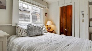 A bedroom with a bed, a window, a lamp, and a wooden door. - Sisters - 1 Block to the Beach! (Cannon Beach)
