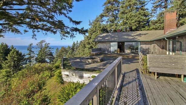 Una casa costera con un balcón que da al mar, rodeada de un bosque frondoso.
