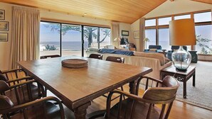 Un salón amplio con una mesa de comedor de madera, asientos cómodos y ventanas grandes con vistas al océano.