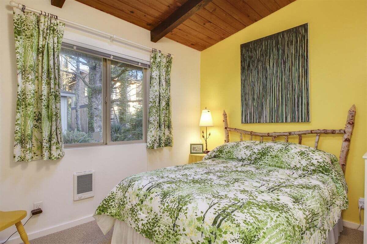 A bedroom with a bed, a window with curtains, a bedside lamp, and a wall-mounted artwork.
