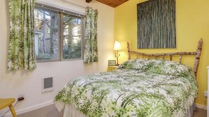 Une chambre à coucher avec un lit, une fenêtre avec des rideaux, une lampe de chevet et une œuvre d’art accrochée au mur.