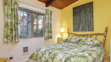 A bedroom with a bed, a window with curtains, a bedside lamp, and a wall-mounted artwork.