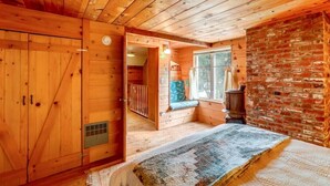 L’intérieur d’un chalet en bois, avec un lit, une fenêtre donnant sur un paysage, un mur en briques et une porte en bois.