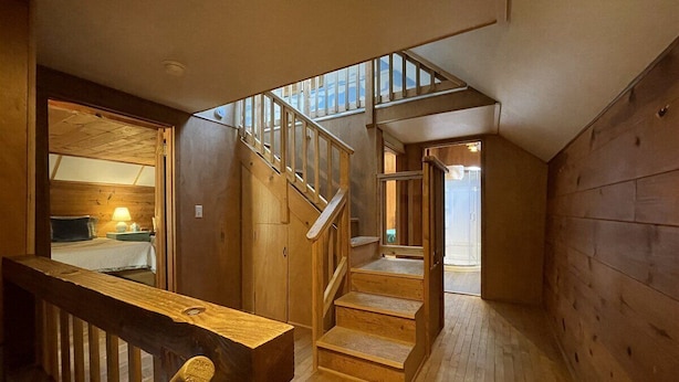 Un escalier en bois mène à une chambre située en mezzanine, avec un plafond en pente et une lucarne visible.