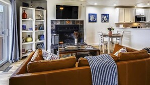 Ein modernes Wohnzimmer mit einer Couch, einem Kamin, einem Fernseher und einer Küchenzeile mit weißen Schränken.