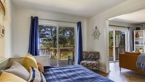 Ein Schlafzimmer mit Bett, Sessel, Sofa und Blick ins Freie durch eine Schiebetür.