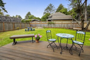 Ein Garten mit einer Holzterrasse, einem Picknicktisch, zwei Stühlen und einem kleinen Tisch mit einem Blumentopf.