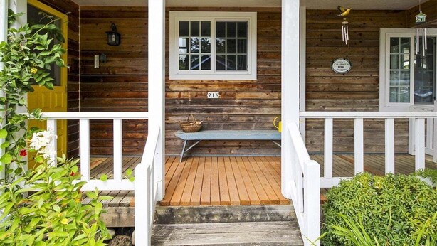 A wooden cabin with a porch, a bench, and a window.