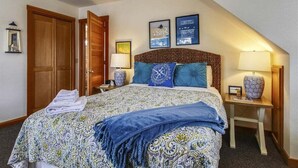 Een hotelkamer met een groot bed, een houten garderobe, twee nachtkastjes met lampen, en een lijst met een afbeelding aan de muur.
