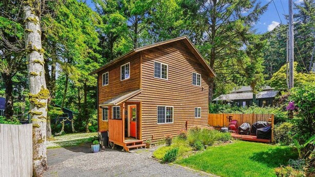 Eine zweistöckige Holzhütte mit Veranda, umgeben von einem gepflegten Garten und Bäumen.