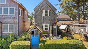 A two-story house with a small front porch, a blue gate, and a garden with various plants and flowers. - Newly Renovated+Fire Table+Steps from Cannon Beach (Cannon Beach)